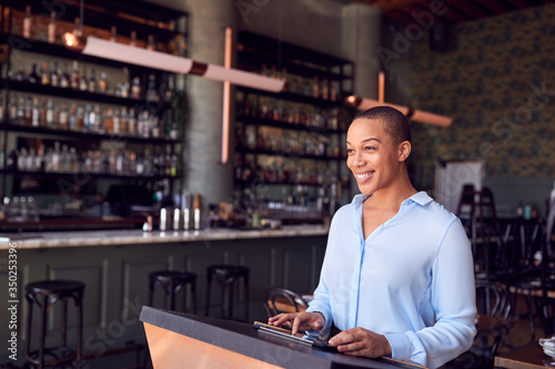 Female Owner Of Restaurant Bar Standing At Counter Using Digital Tablet photo