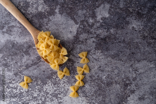 Top view of a wooden spoon full of pasta, farfalle type, on a dark marble background.