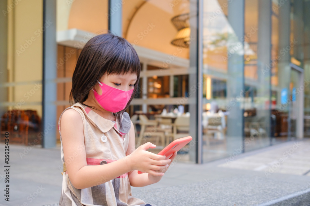 Asian child wearing mask and using cell phone in city