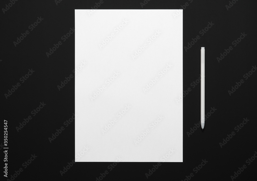 a blank sheet of paper and a pen on a black table, top view - template for any text or inscription a blank sheet of paper and a pen on a black table, top view - template for any text or inscription