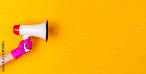 Hand in pink protective rubber glove with megaphone isolated on yellow studio background with copyspace. Gesturing, holding, presenting things. Negative space for your advertising. Showing, pointing.