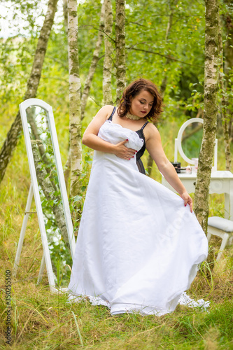 A beauty woman trying on a wedding dress in front of mirror in the forest, morning of the bride, natural beauty