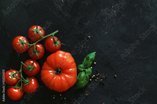 Fresh tomatoes on a black background with spices. Top view