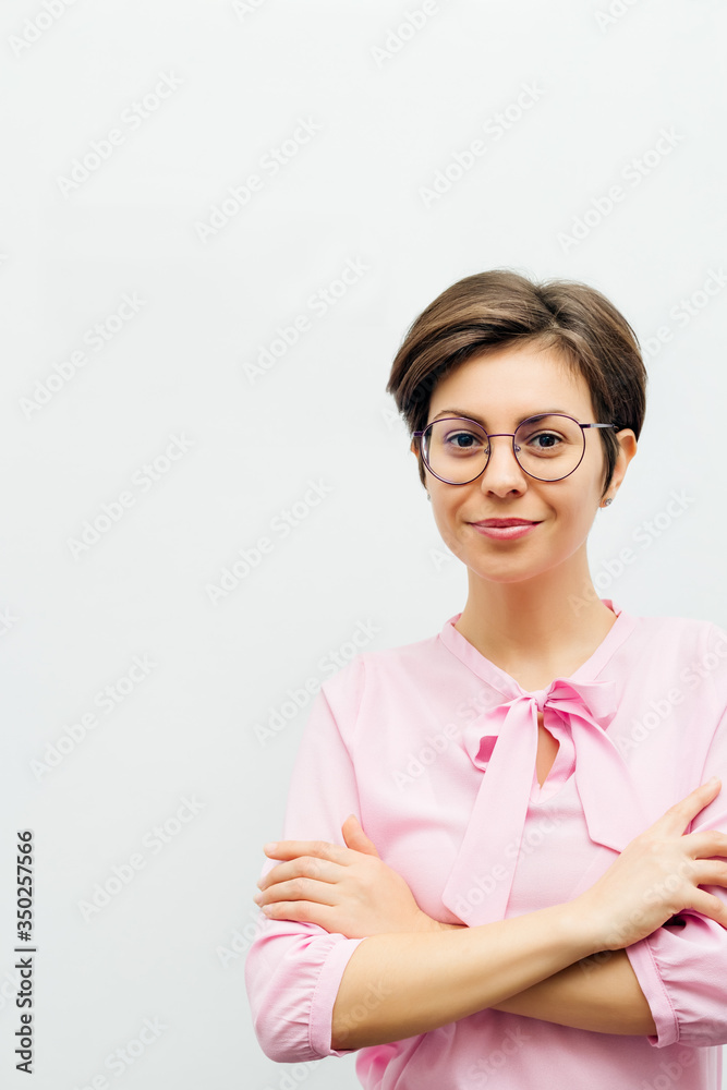 An attractive smiling young brunette stands with her arms folded against a white wall An attractive smiling young brunette stands with her arms folded against a white wall