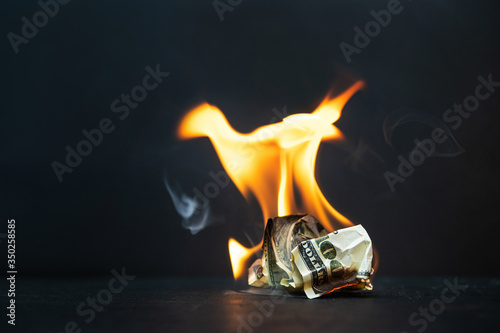 Crumpled dollar bills burning fire on a dark background