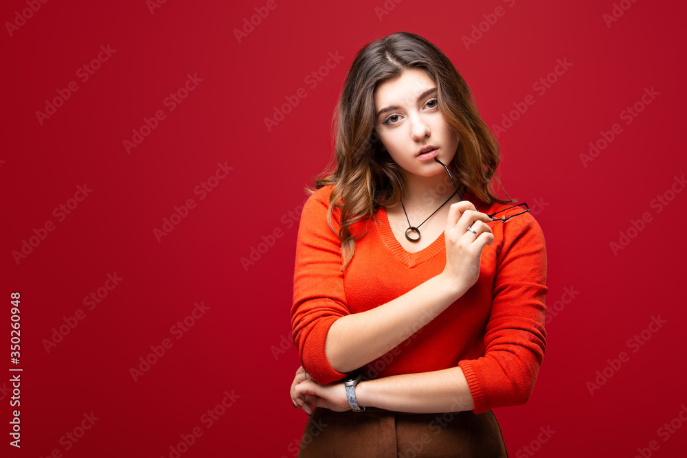 Young girl student or business woman with glasses in hands isolated on a red background. Skeptical look and mood