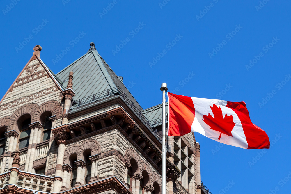 The waving Canadian flag at Old City Hall in background in Toronto, Canada. Toronto is the provincial capital of Ontario and the most populous city in Canada. 
