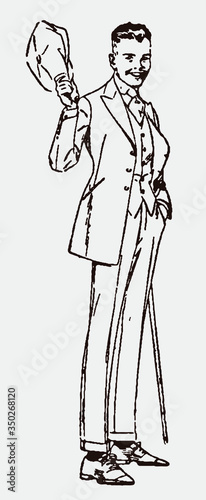 Standing and smiling young man from the early 20th century in a suit, holding a walking stick and greeting with his cap