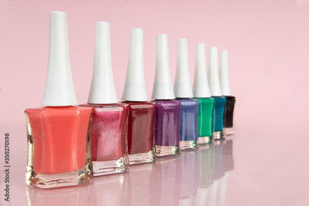 Group of bright nail polishes in different colors on pink background