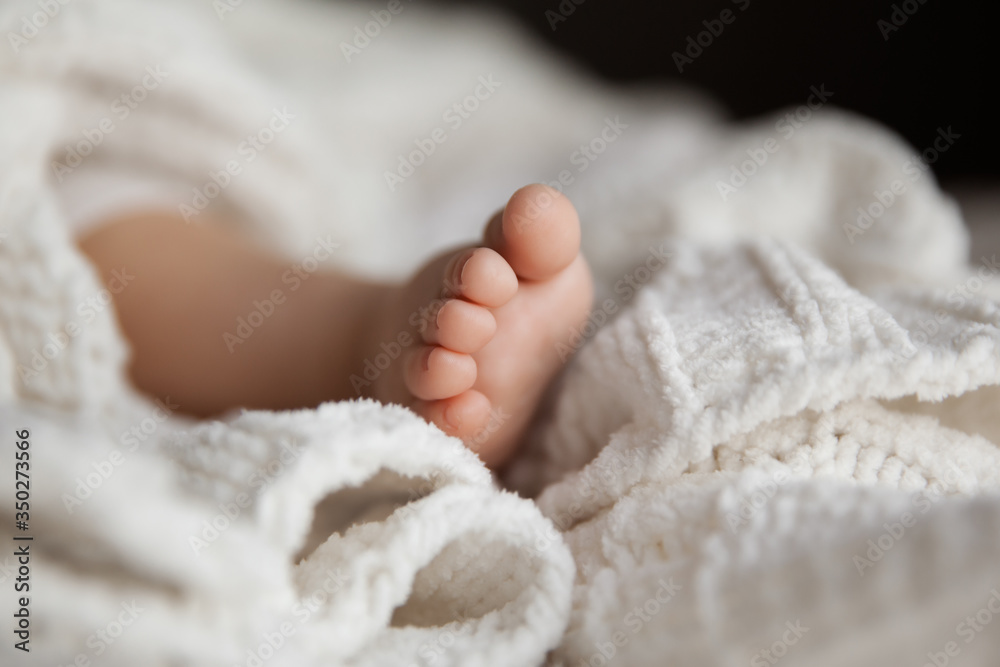 Closeup of infant leg under white soft blanket, tiny toes of baby girl Closeup of infant leg under white soft blanket, tiny toes of baby girl