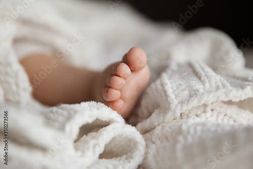 Closeup of infant leg under white soft blanket, tiny toes of baby girl