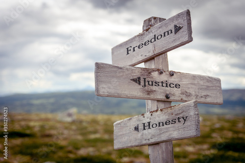 freedom justice honesty text engraved on wooden signpost outdoors in nature.