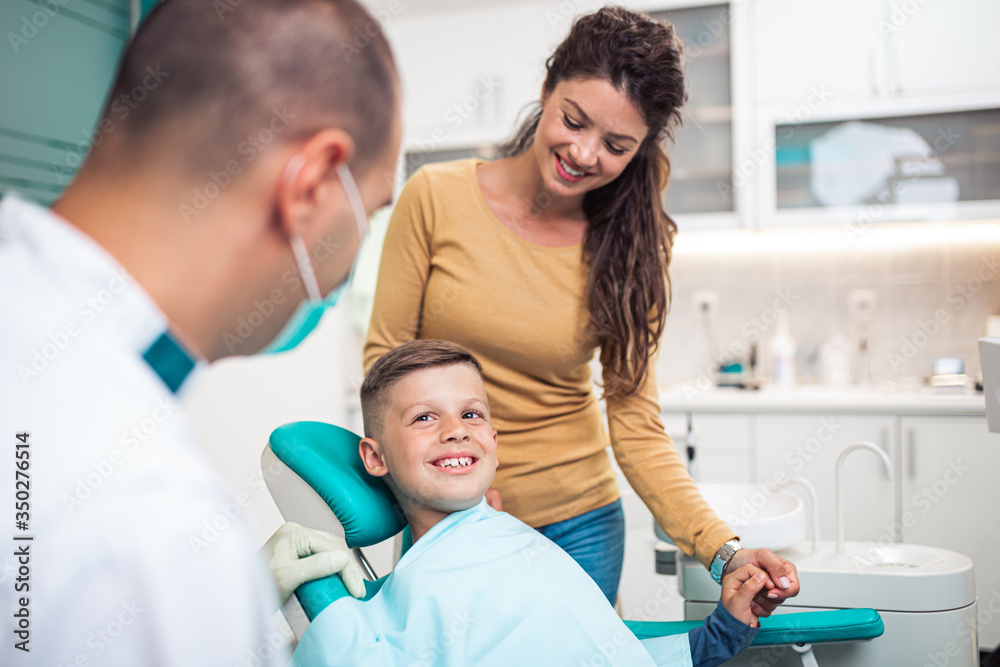 Obraz premium Cute little boy sitting on dental chair and having dental treatment. His mother is with him.