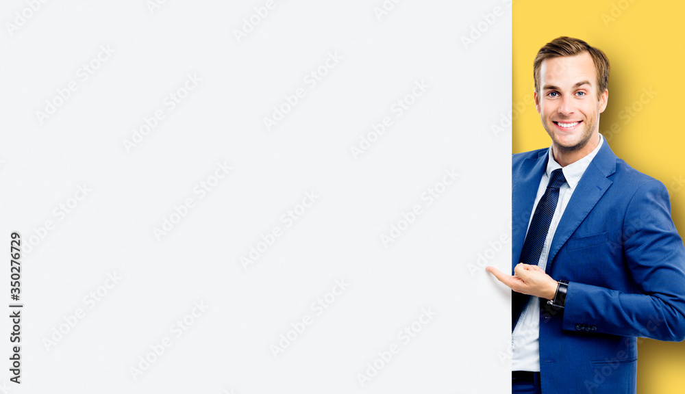 Confident happy businessman showing blank sign board or banner, standing against yellow color background. Copy space for some slogan or text. Confident happy businessman showing blank sign board or banner, standing against yellow color background. Copy space for some slogan or text.