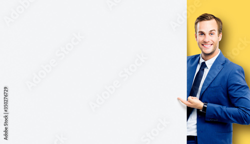 Confident happy businessman showing blank sign board or banner, standing against yellow color background. Copy space for some slogan or text.