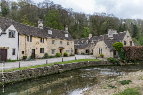 English village street near the river, typical houses with stone facades and dark roofs, Castle Combe, England