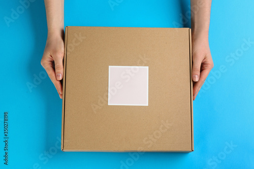 Woman holding cardboard box on light blue background, top view © New Africa