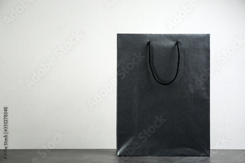 Black shopping paper bag on table against light background. Space for text