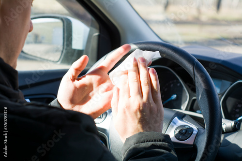 antibacterial treatment of the car, a young male driver wipes his hands with an antibacterial cloth, view from the back seat © Anzhelika