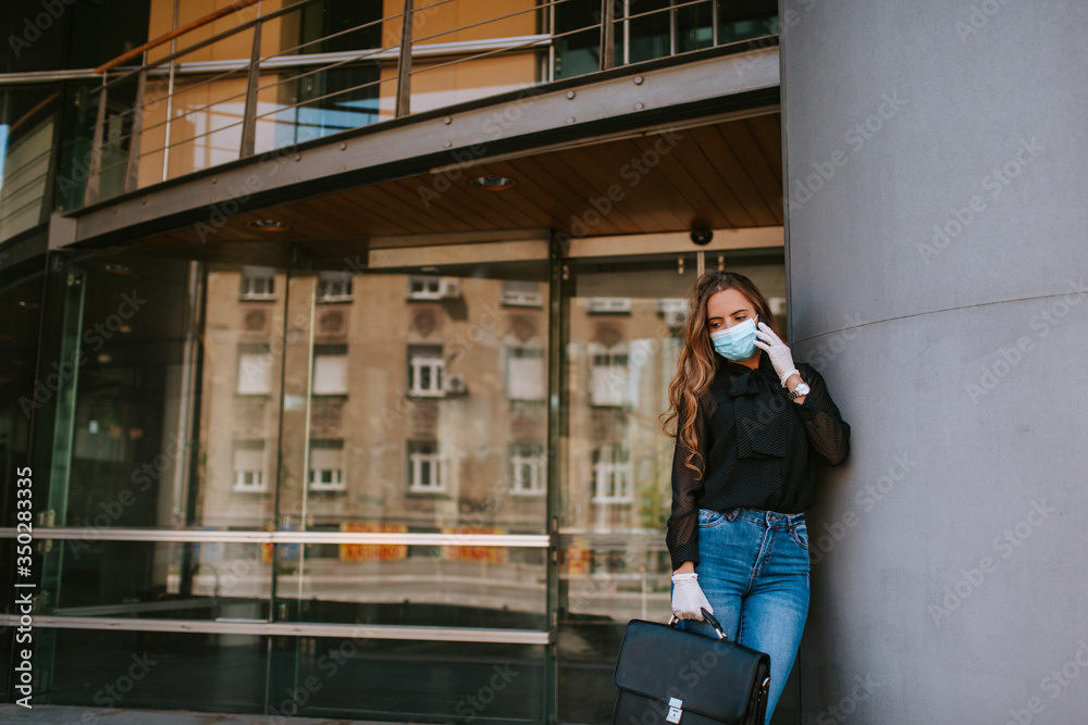 A beautiful attractive caucasian businesswoman with a mask and gloves stands in front of the company. COVID - 19 virus protection