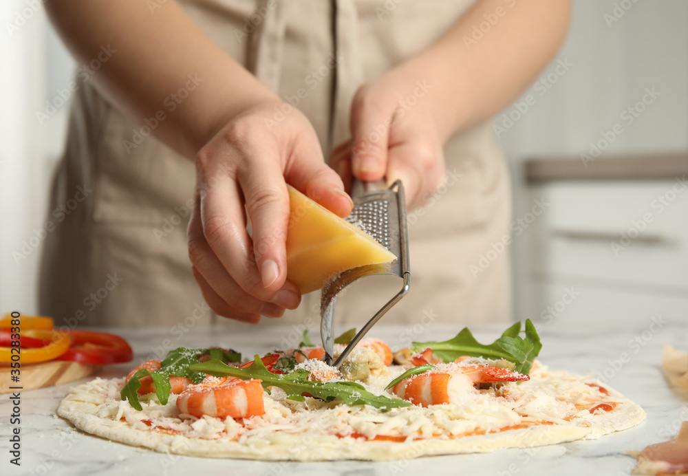 Woman grating cheese onto pizza at white marble table, closeup