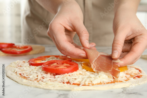 Woman adding prosciutto to pizza white marble table, closeup