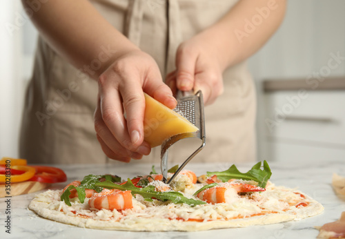 Woman grating cheese onto pizza at white marble table, closeup