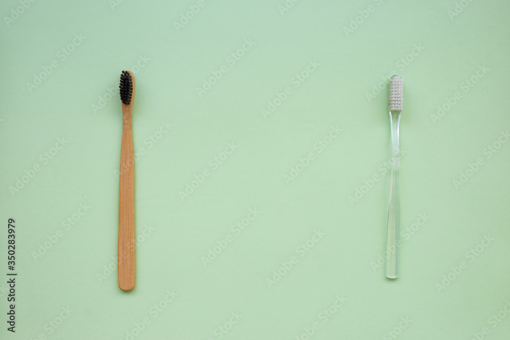 Two toothbrushes: natural bamboo and plastic on a green paper background Two toothbrushes: natural bamboo and plastic on a green paper background