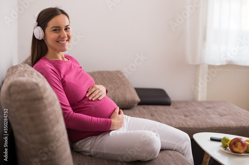 Beautiful pregnant woman enjoys listening music at her home. 