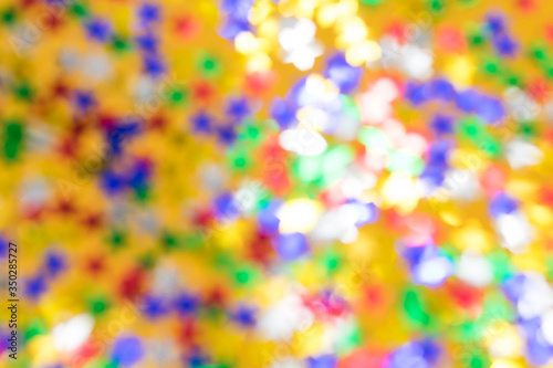 Blurred background with multicolored sparkles and lights on a yellow background