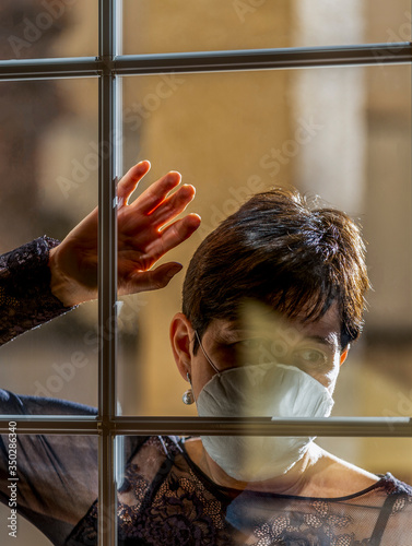 Corona virus. Woman sick with Covid wearing a protective mask and recovering at home from the disease after quarantine looking out the window at Patient Street in isolation to prevent infection. 