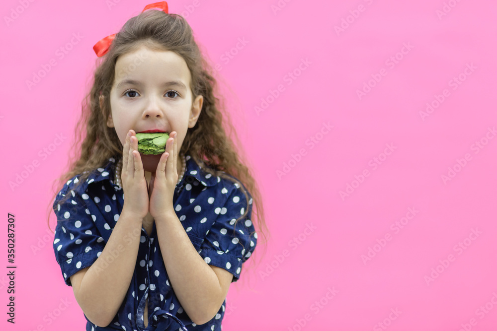Small girl with curly hair posing for a photo holding green macaroon. Small girl with curly hair posing for a photo holding green macaroon.