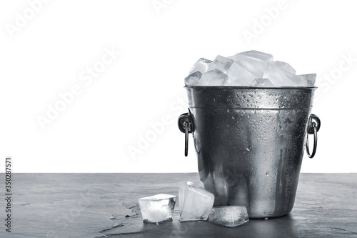 Metal bucket with ice cubes on table against white background