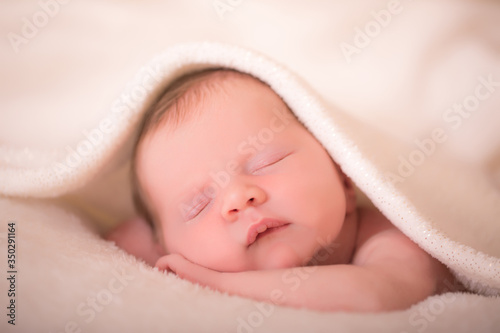 Newborn child relaxing in bed after bath or shower. Nursery for children. Textile and bedding for kids. Little girl sleeping on soft white blanket.