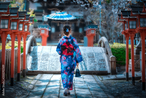 Back view of asia woman with kimono and Japanese umbrella against sakura flower background. © chanchai