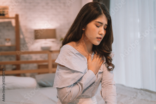 Portrait of 20s young Asian woman having difficulty breathing in bedroom at night. Shortness of breath, asthma, difficult to breathe problems. Corona Virus symptoms.