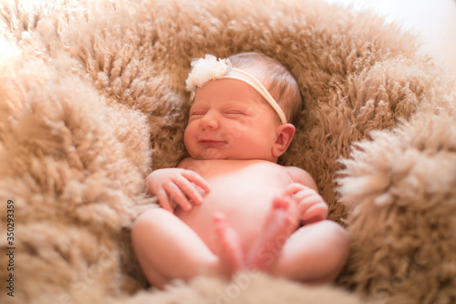 Lovely newborn girl sleeping on pink blanket with bare feet. Baby newborn with headband sleeping covered on white woolen blanket.