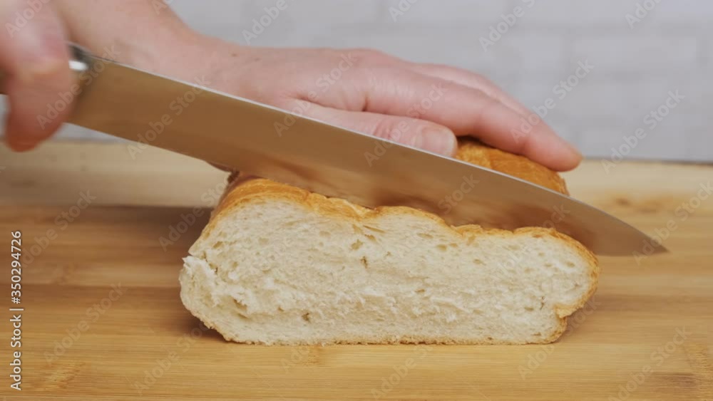 Woman cuts bread with knife on wooden board closeup.