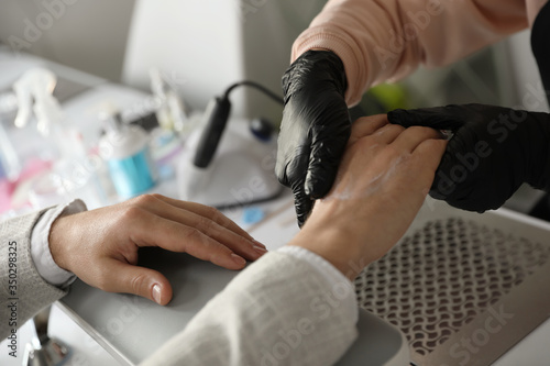 Professional manicurist applying cream on client s hand in beauty salon  closeup
