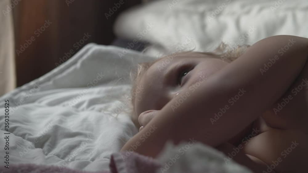 Toddler girl is staying in bed and rubbing face after waking up the morning. She does not want to get up Toddler girl is staying in bed and rubbing face after waking up the morning. She does not want to get up