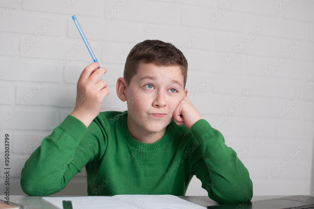pupil confused. boy focused on hometask holding pen straight sitting at table in light room