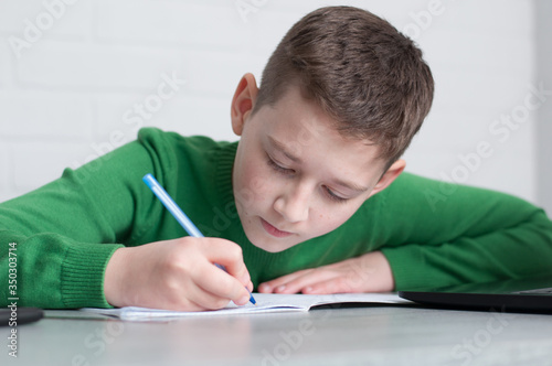 pupil boy focused on hometasks writing in copybook sitting at table in light room
