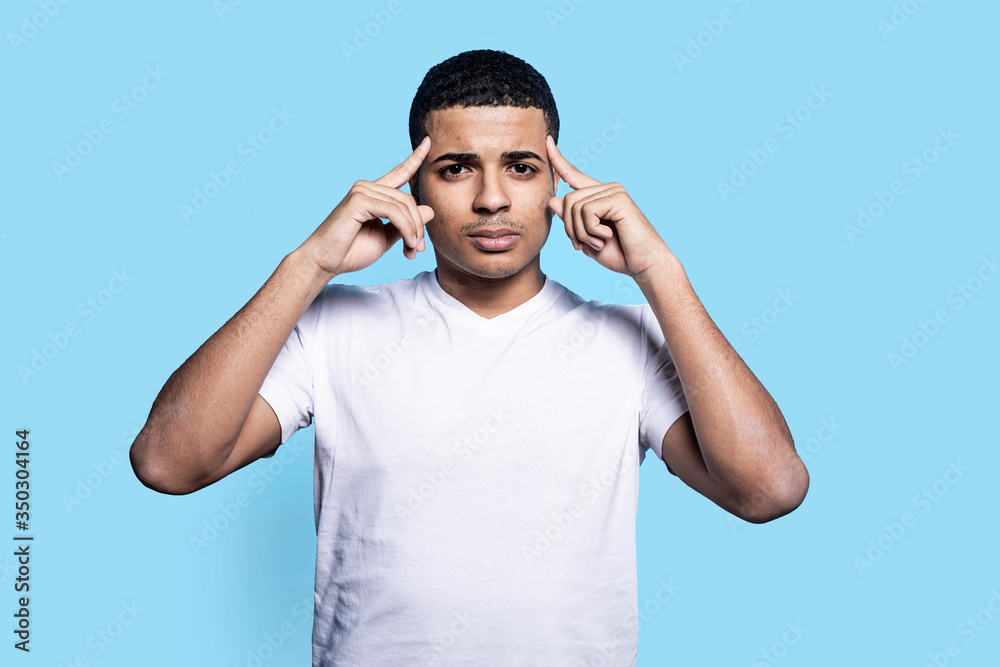 Horizontal portrait of black man in white t-shirt with fingers on temples, isolated on blue background