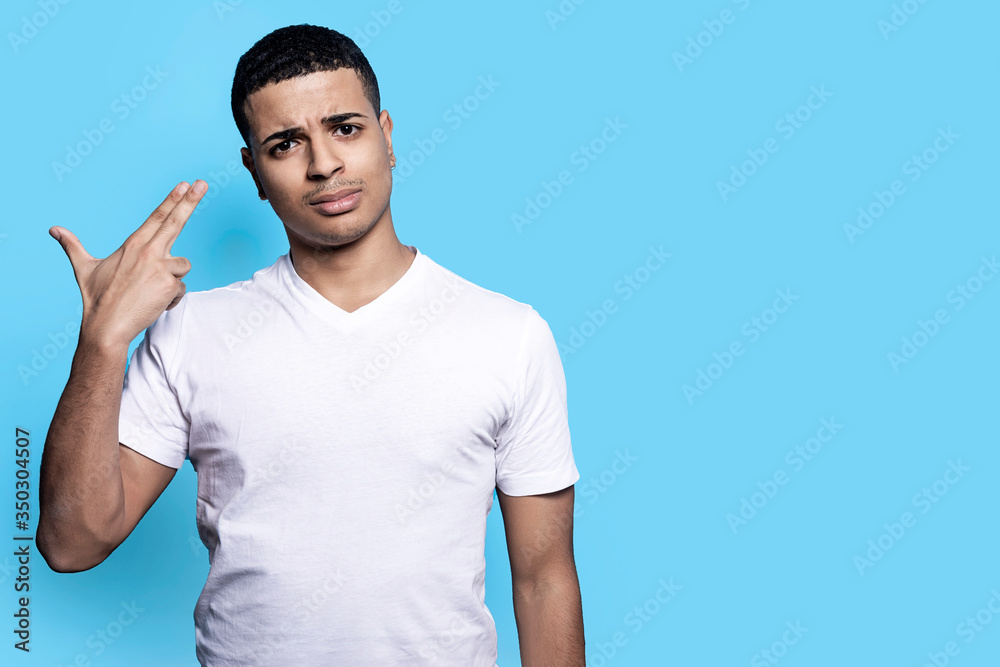 Young displeased man in casual clothes posing isolated on blue background in studio while pointing fingers to head as if he about shoot himself Young displeased man in casual clothes posing isolated on blue background in studio while pointing fingers to head as if he about shoot himself