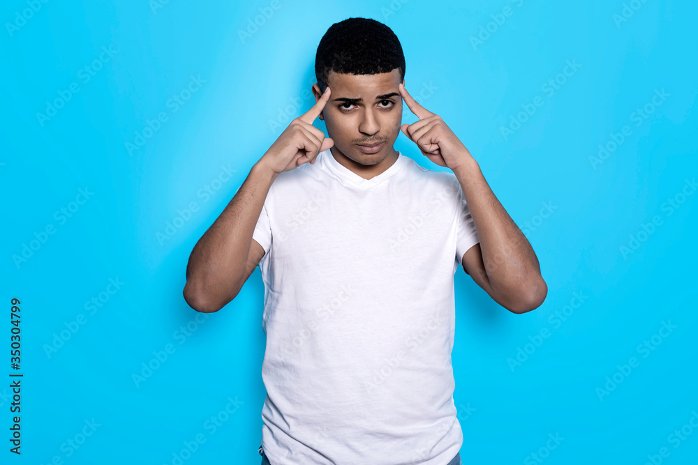 Horizontal portrait of black man in white t-shirt with fingers on temples, isolated on blue background Horizontal portrait of black man in white t-shirt with fingers on temples, isolated on blue background