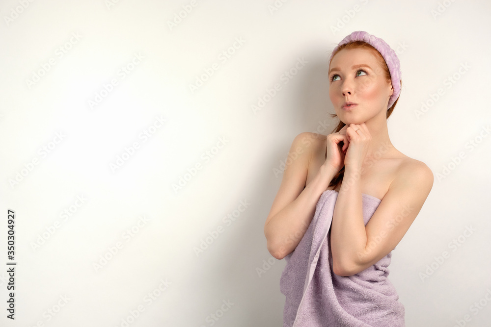 Cute red-haired girl is standing on a white background in a towel and is dreamily looking up clutching her hands to her chest Cute red-haired girl is standing on a white background in a towel and is dreamily looking up clutching her hands to her chest