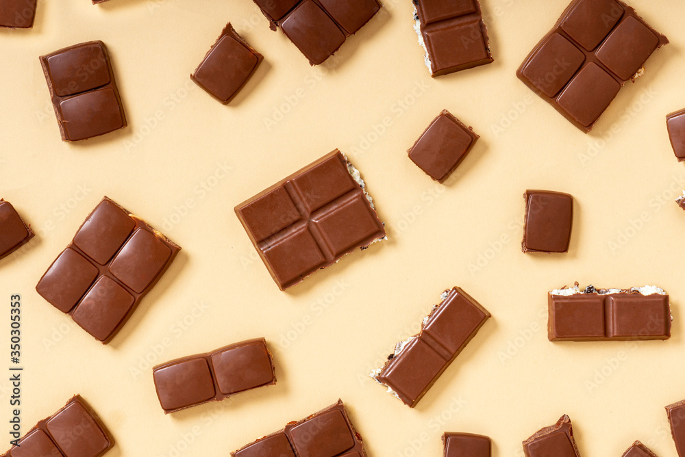 Pieces of milk chocolate on a beige background top view. Chocolate background, sweet food. Pieces of milk chocolate on a beige background top view. Chocolate background, sweet food.