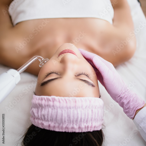 Girl receiving darsonval procedure electric massage at beauty salon. Hardware cosmetology. Selective focus. photo