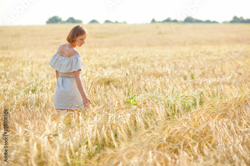 A young girl with a straw hat on her head is dancing in a wheat field. Runs his hand over the ears. Stands with his back to the camera.