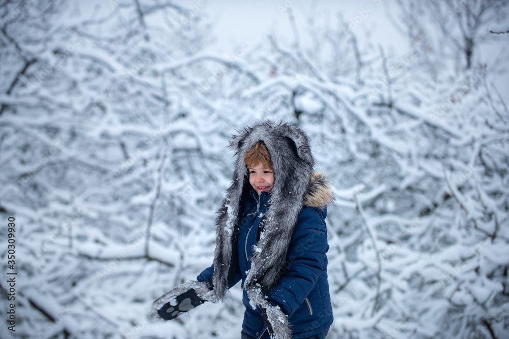 Winter Kids and nature. Cute child in Winter park trees covered with snow. Outdoor portrait of cute baby kid in cold sunny winter weather in park.